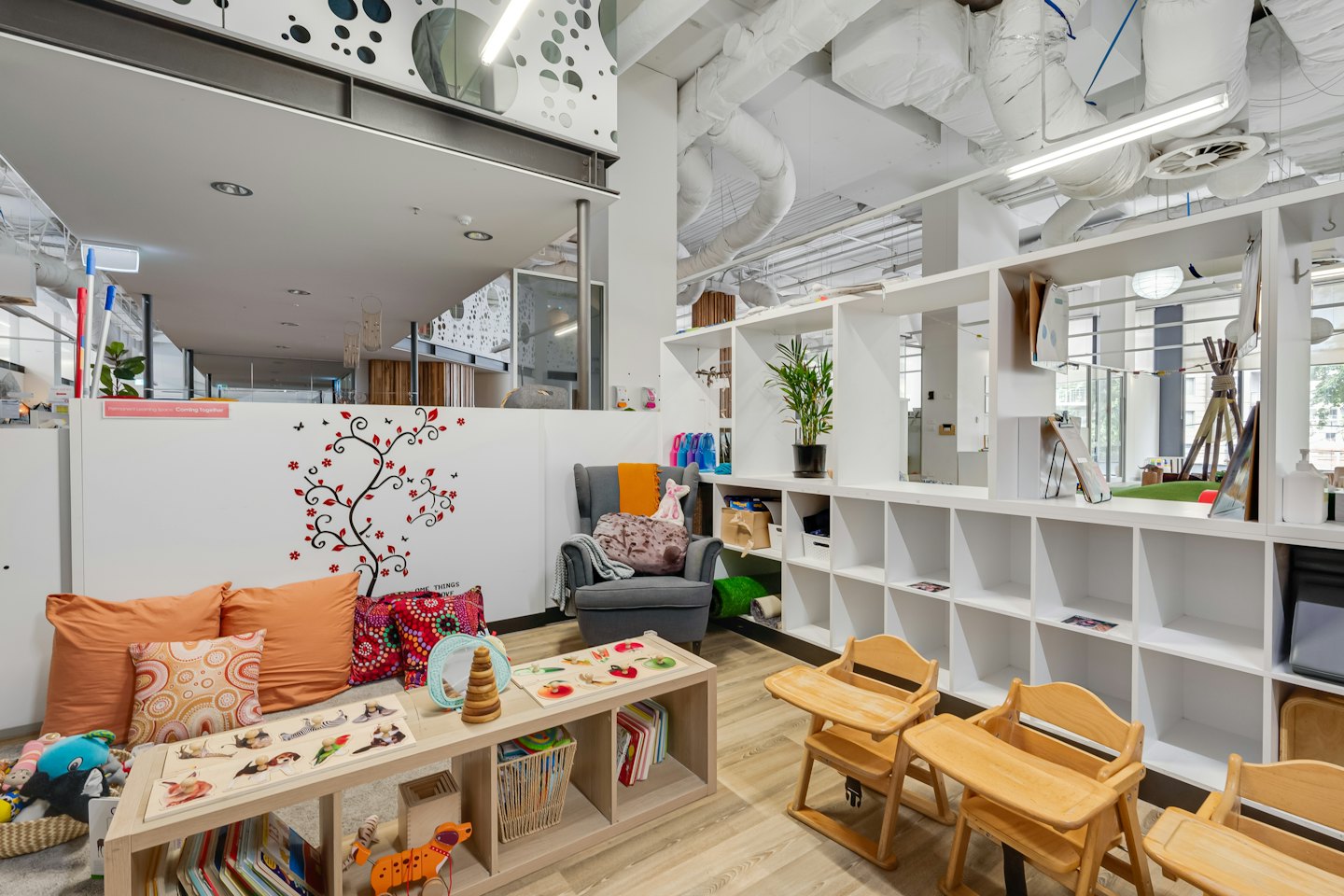 Moderner Kinderzimmer mit Holztischen, Spielzeug und Kissen.